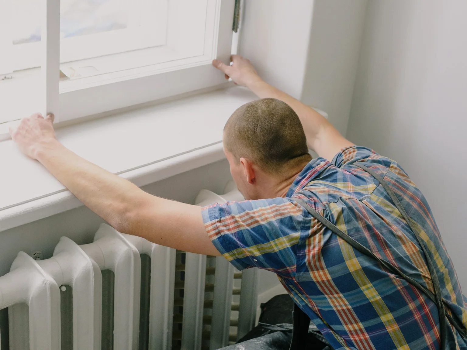 Worker checking and sealing a window frame during scheduled home upkeep