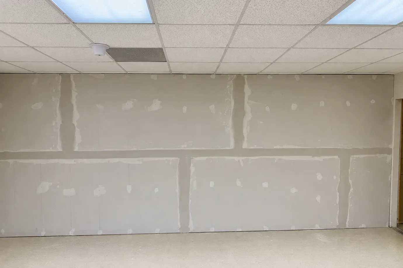 Commercial interior drywall repair with taped and mudded joints beneath a suspended ceiling